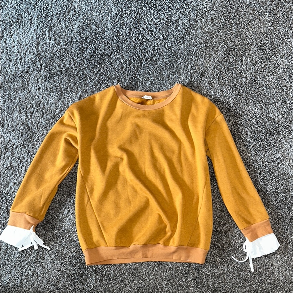 Burnt orange crewneck sweater with white fabric ruffles on the sleeves